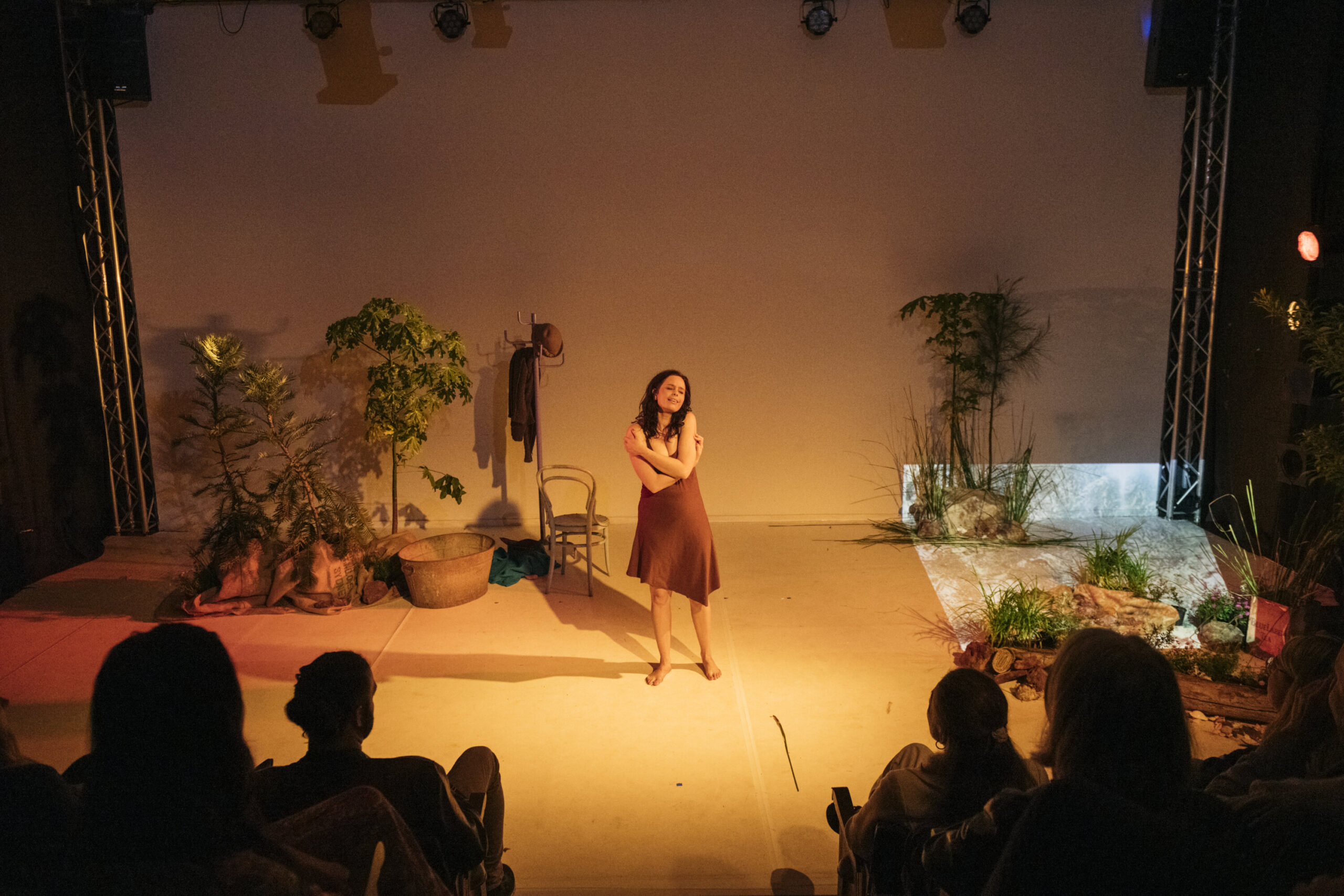 Sandy Greenwood stands in the centre of a stage which is lit orange. Trees stand either side of the artist.