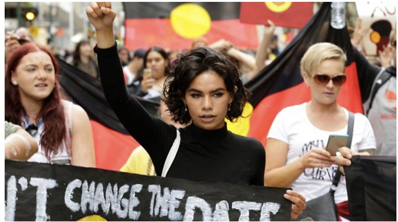 An crowd parade for First Nations rights. A woman stands in the centre with her first up holding a sign.